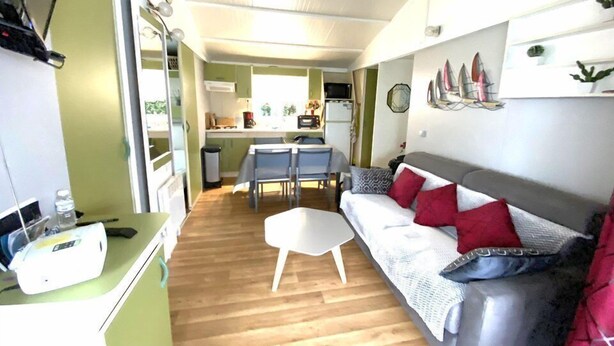 A compact living space with a kitchenette, a dining area, and a seating area with a sofa and chairs. - Charming chalet located in a 4-star  campsite - 6 people (GUIDEL-PLAGES)