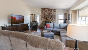 A living room with a stone fireplace, a television, and a large window with curtains. - Mingus Mountain Vista: Views, Shopping, Relaxation. 20 Minutes to Sedona  (Cottonwood)