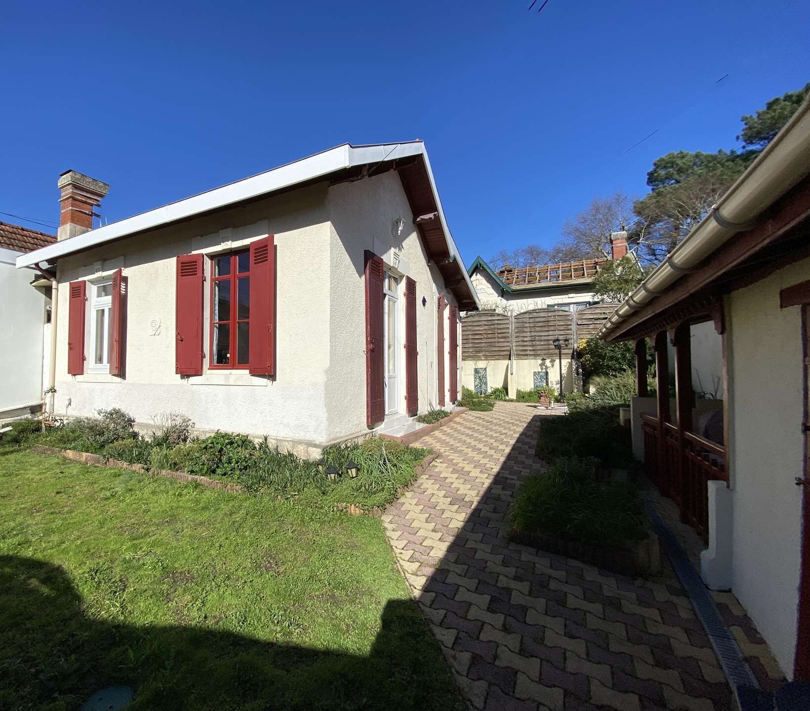 Un bâtiment avec un chemin pavé menant à une porte, entouré de verdure et sous un ciel bleu dégagé.