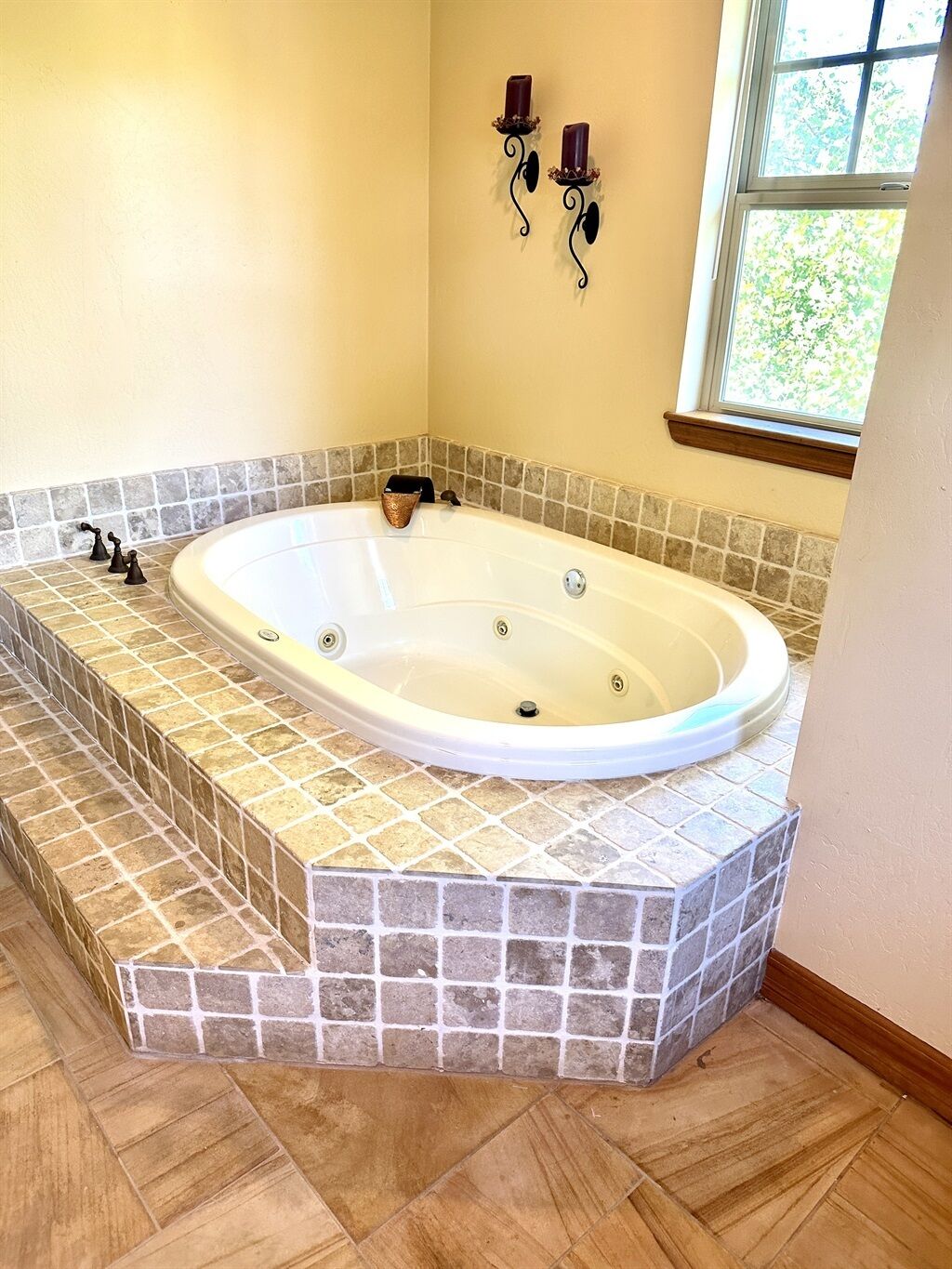 Ein Badezimmer mit freistehender Badewanne, gefliesten Wänden und einem Fenster mit Blick ins Grüne.