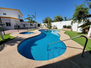Ein Pool mit gebogener Form, umgeben von einer gepflasterten Terrasse und einer kleinen Rasenfläche.