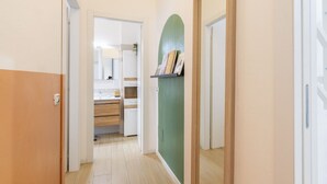 Un pasillo con una puerta de madera, una pared verde con un estante, y una zona de cocina al fondo.