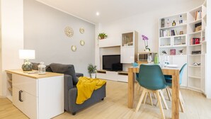 Una sala de estar moderna con un sofá, una mesa de centro, un televisor, un comedor con sillas y una estantería.