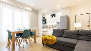 Una sala de estar moderna con un sofá, una mesa de comedor con sillas y una cocina al fondo.