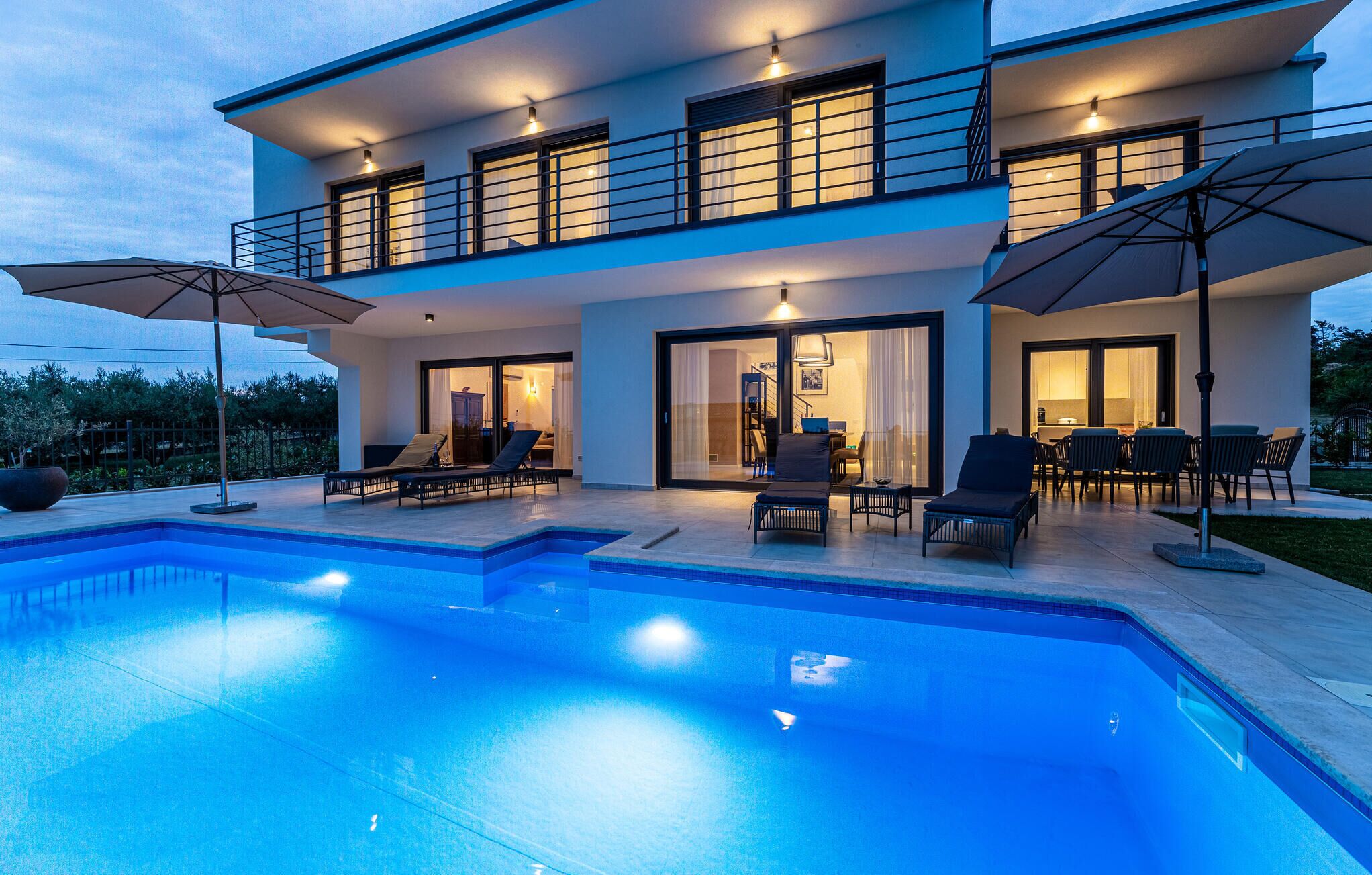 Une maison moderne à deux étages, dotée d’une piscine, d’un espace extérieur aménagé et d’un intérieur bien éclairé.