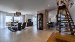 Uma sala de estar ampla com uma mesa de jantar, cadeiras, um sofá, uma televisão e uma escada.