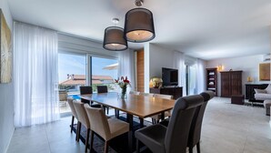 Uma sala de estar ampla com uma grande mesa de jantar, assentos confortáveis, televisão e vista para o exterior.