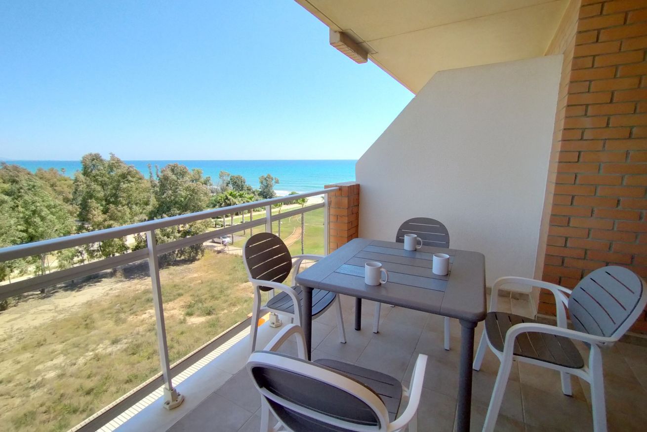 A balcony with a table and chairs, overlooking a coastal landscape.