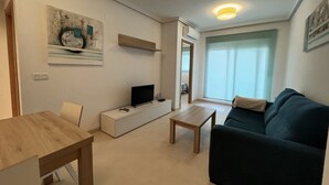A modern living room with a sofa, a coffee table, a TV on a white cabinet, and a painting on the wall.
