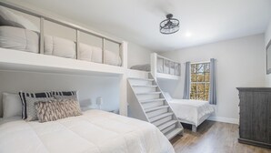 Un dormitorio con una cama litera, una escalera, una ventana con cortinas y un armario de madera.