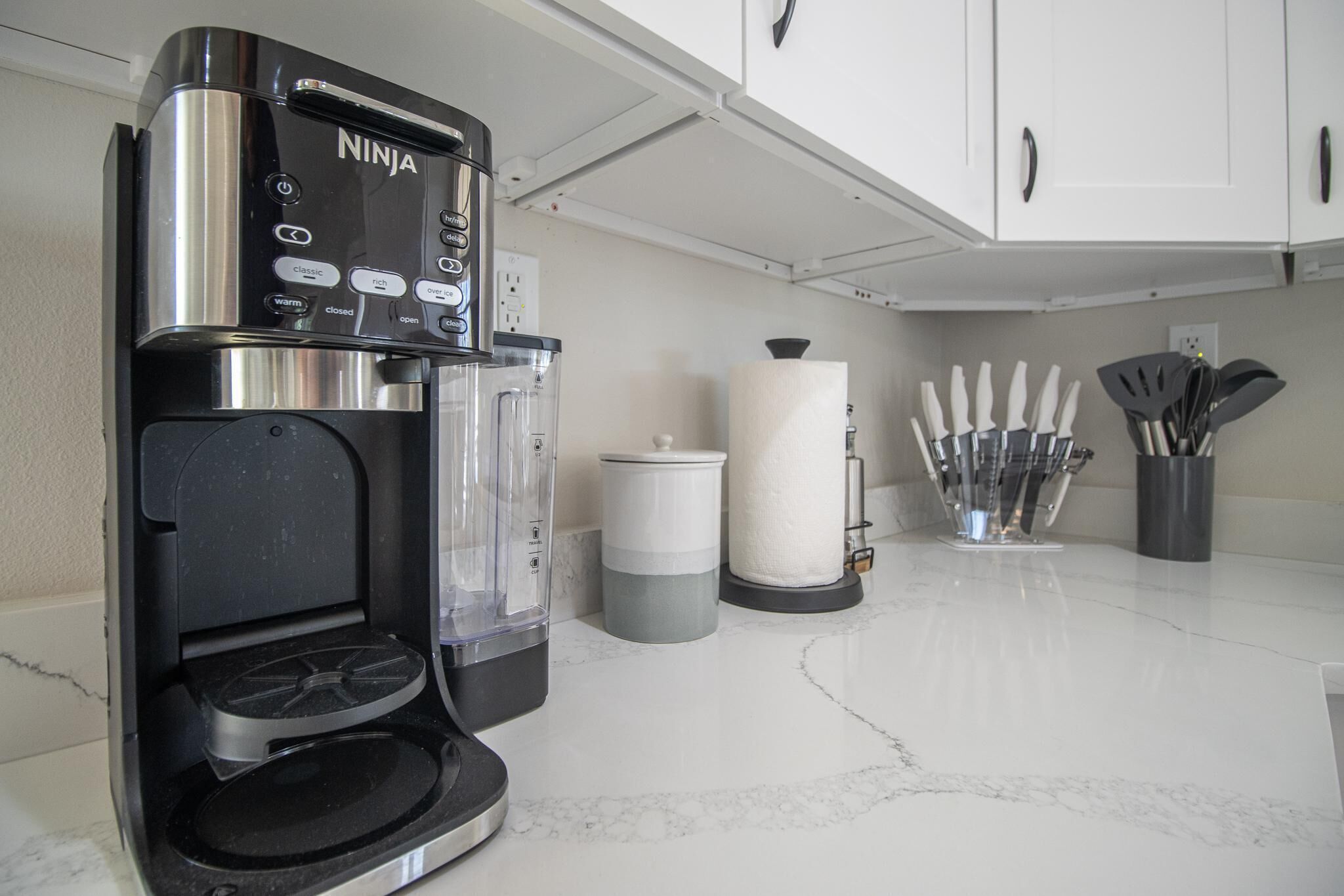 A kitchen with a coffee maker, a trash can, a paper towel holder, and a knife block.