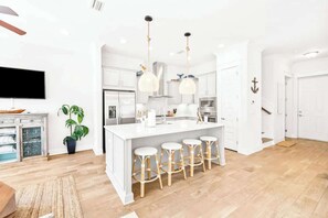 A modern kitchen with white cabinetry, a central island with stools, and pendant lighting.