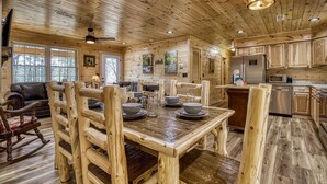 A rustic cabin interior with a wooden dining table set for four, surrounded by wooden chairs. A refrigerator and microwave are visible in the kitchen area. - Hilltop Hideaway - 3 Bedroom 2 Bath - Private! (Sevierville)