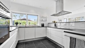 A modern kitchen with white cabinets, a black countertop, a stainless steel range hood, and a window with a view of greenery outside.