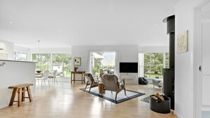 A spacious living area with a wooden floor, a fireplace, a TV, and a dining area with chairs and a table.