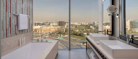 A modern bathroom with two sinks, a large mirror, and a view of a cityscape through floor-to-ceiling windows.