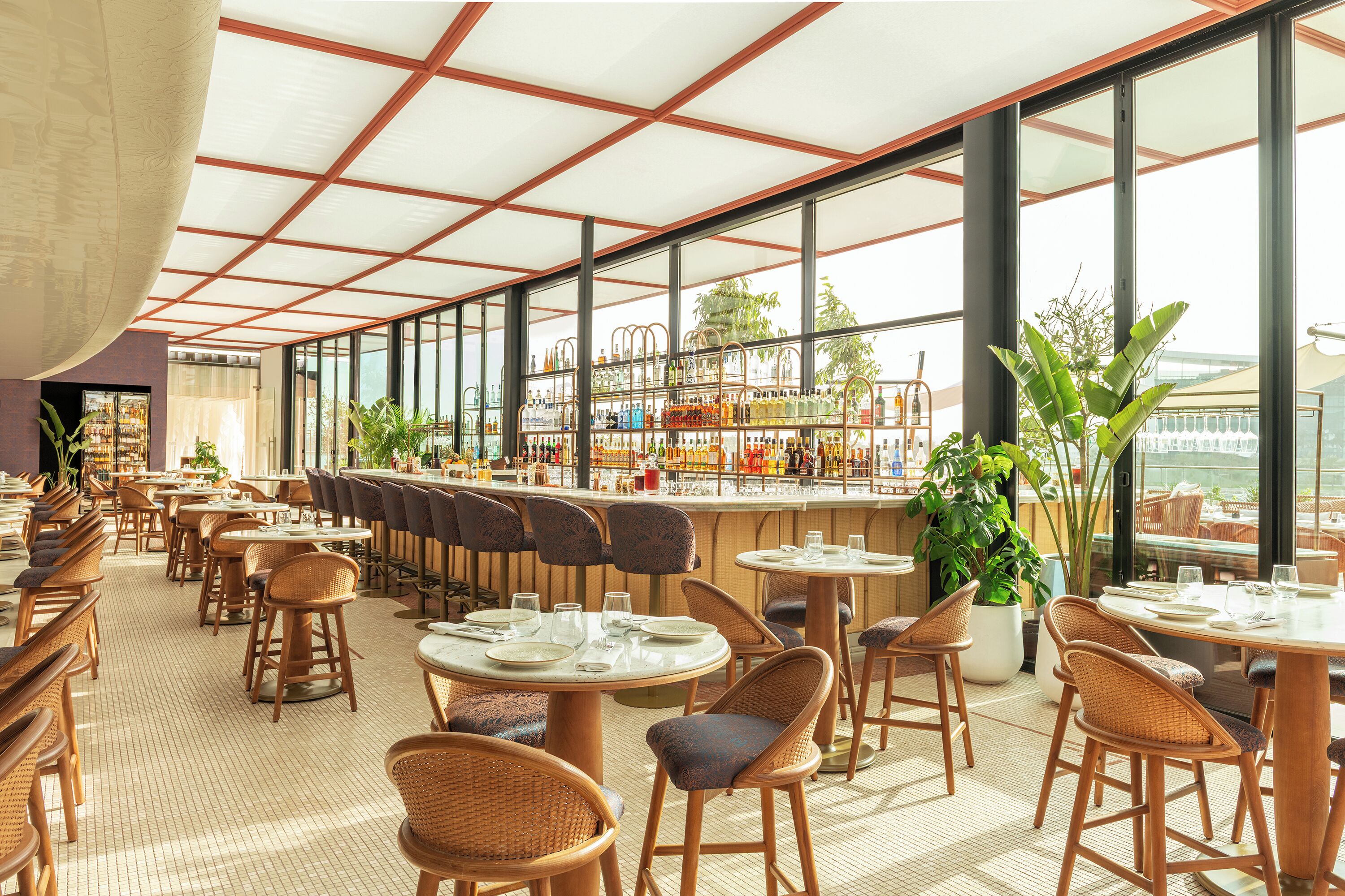 A spacious restaurant with high ceilings, large windows, and a variety of seating arrangements including bar stools and round tables.
