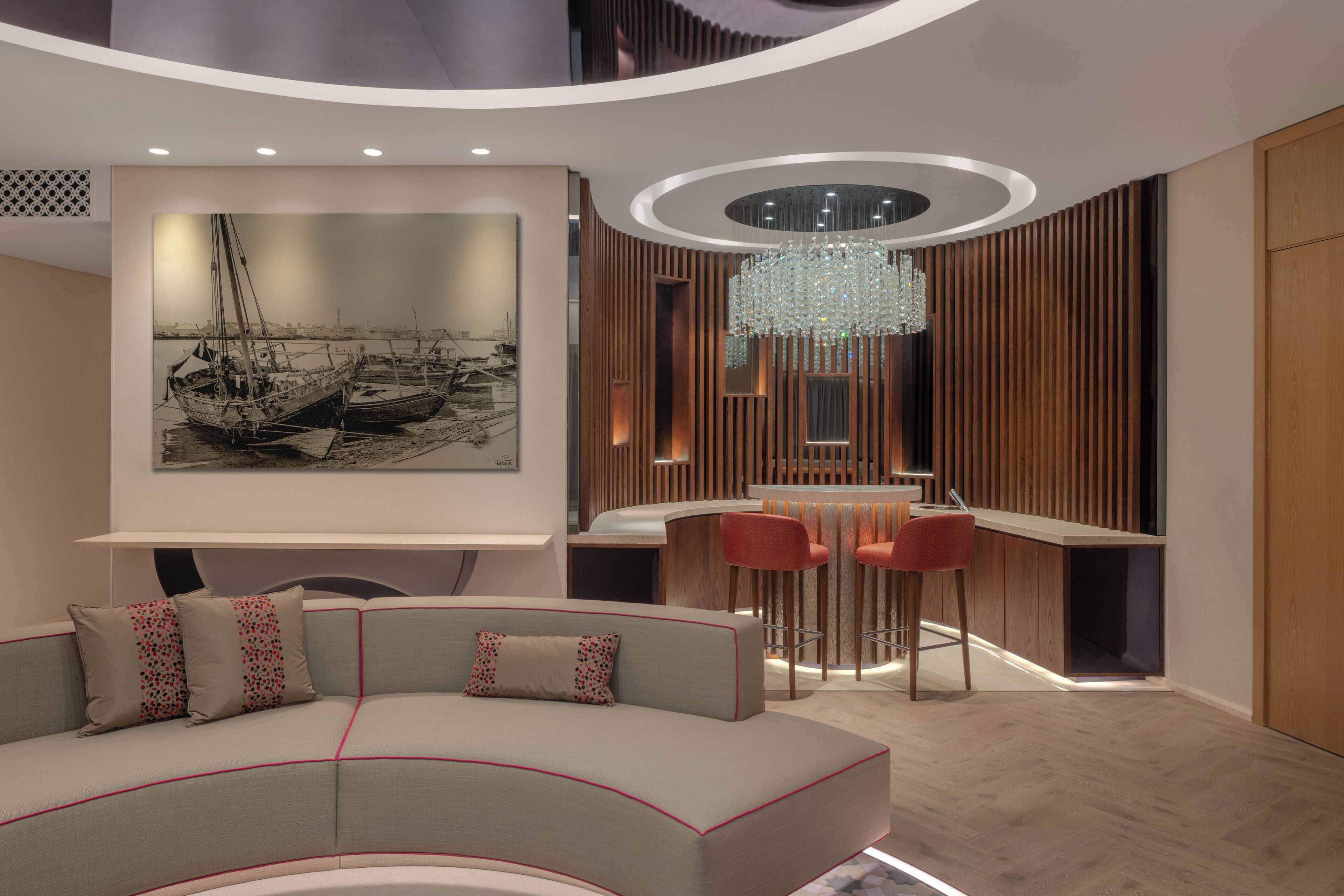 A modern interior with a curved sofa, a bar area with red chairs, and a large framed picture of boats on the wall.
