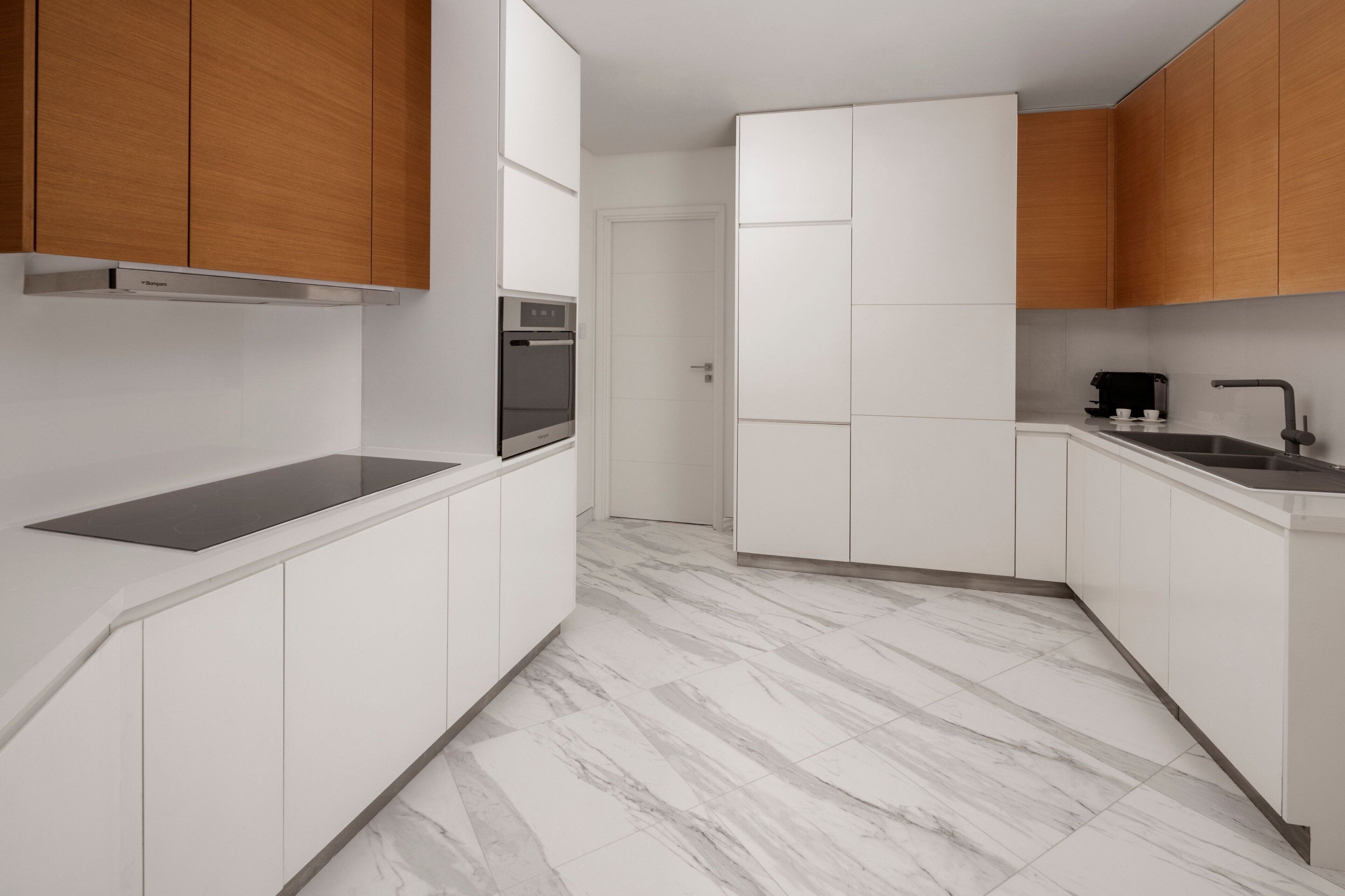 Uma cozinha moderna com armários brancos, piso de mármore e forno embutido.