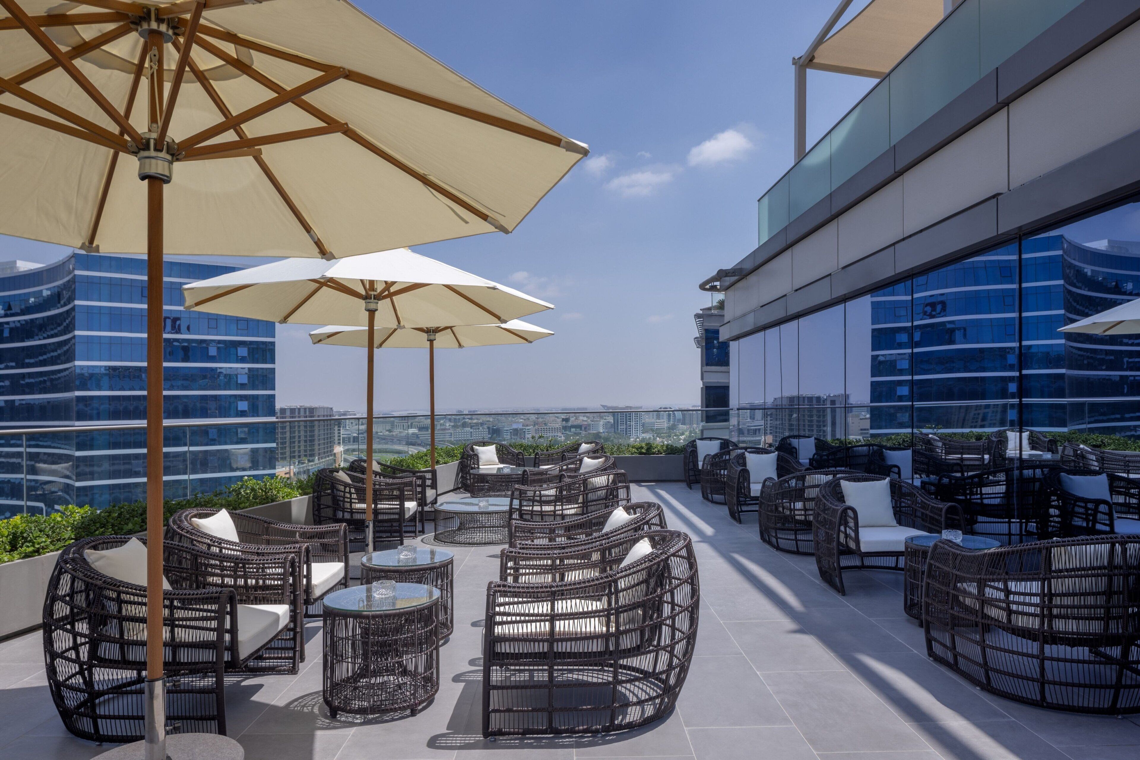 A rooftop terrace with wicker furniture and umbrellas, overlooking a cityscape.