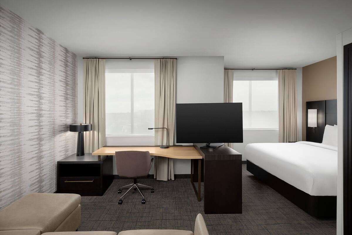A hotel room with a bed, desk, chair, TV, and a small sofa.