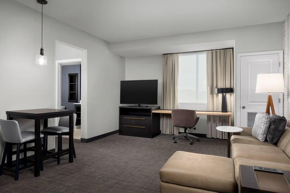 A hotel room with a desk, television, sofa, and a dining area.