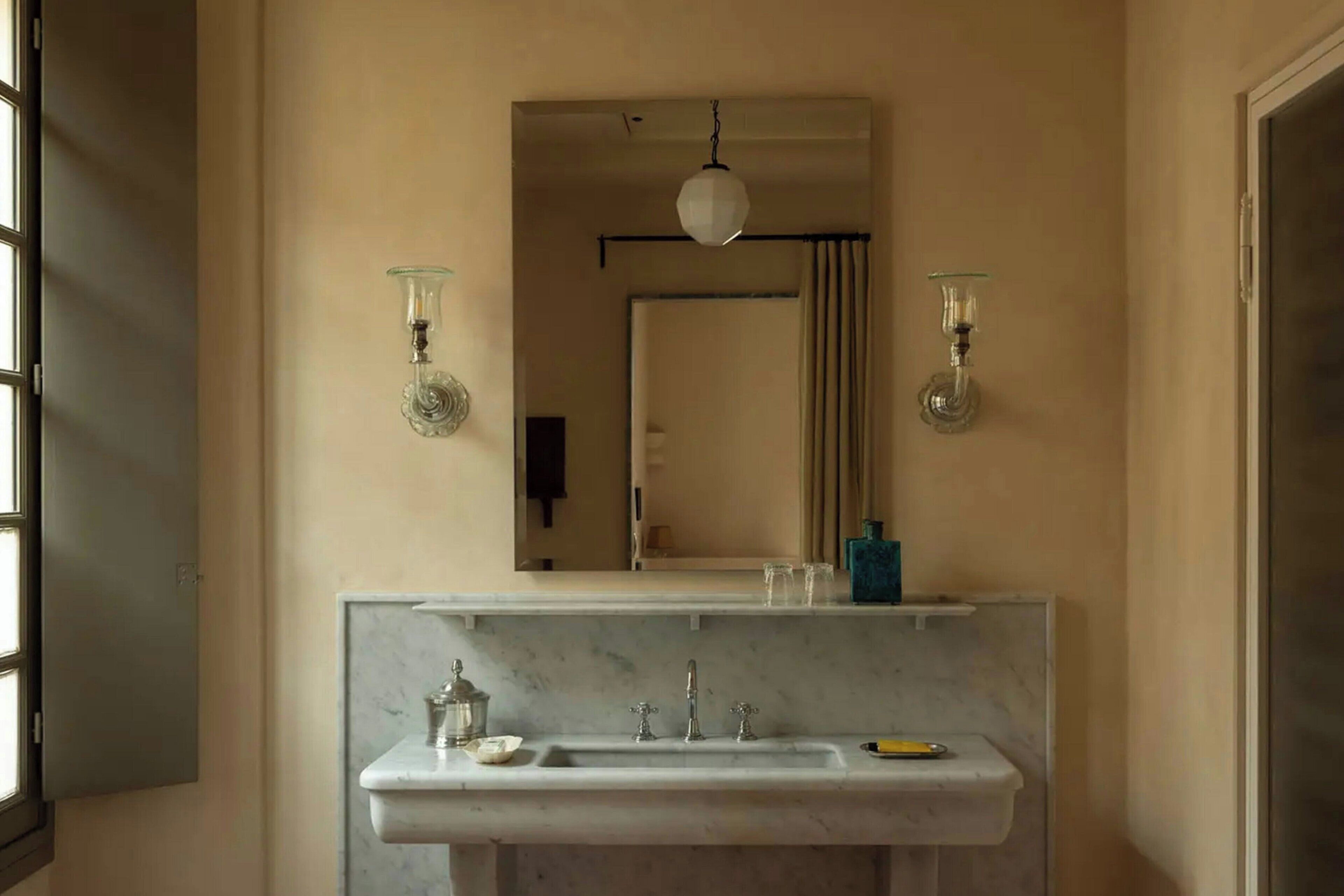 A bathroom with a marble sink, two wall-mounted light fixtures, a mirror, and a hanging light.