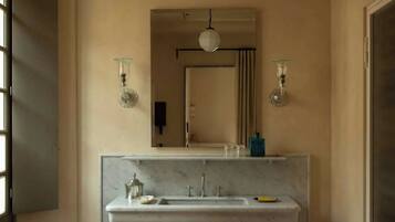 A bathroom with a marble sink, two wall-mounted light fixtures, a mirror, and a hanging light.