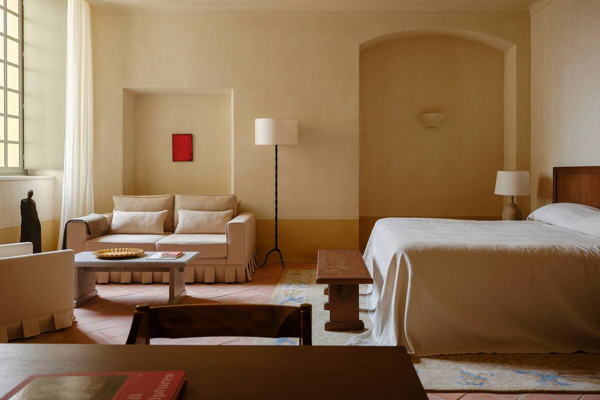 A hotel room with a bed, a sofa, a small table, a lamp, and a red artwork on the wall.