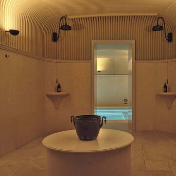 A spa room with a bathtub, a round table with a pot, and wall-mounted shelves with bottles.
