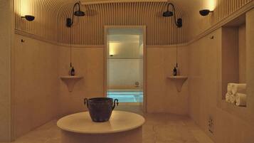 A spa room with a bathtub, a round table with a pot, and wall-mounted shelves with bottles.