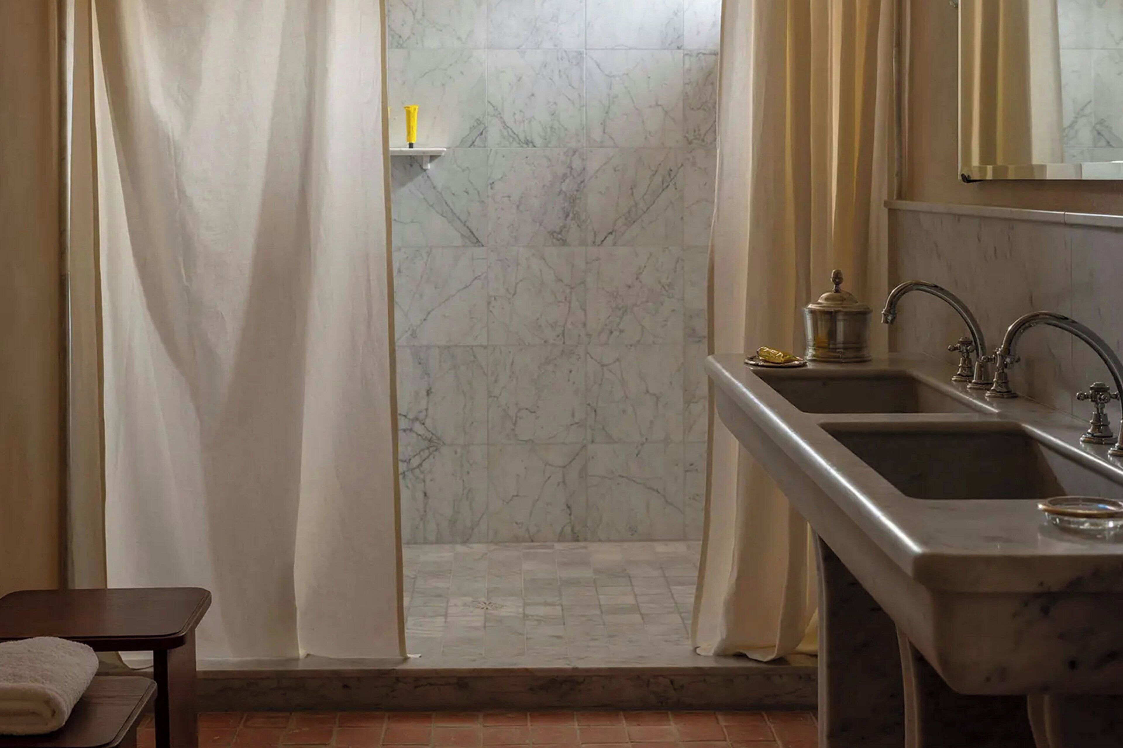 A bathroom with a shower, two sinks, a mirror, and a towel rack.