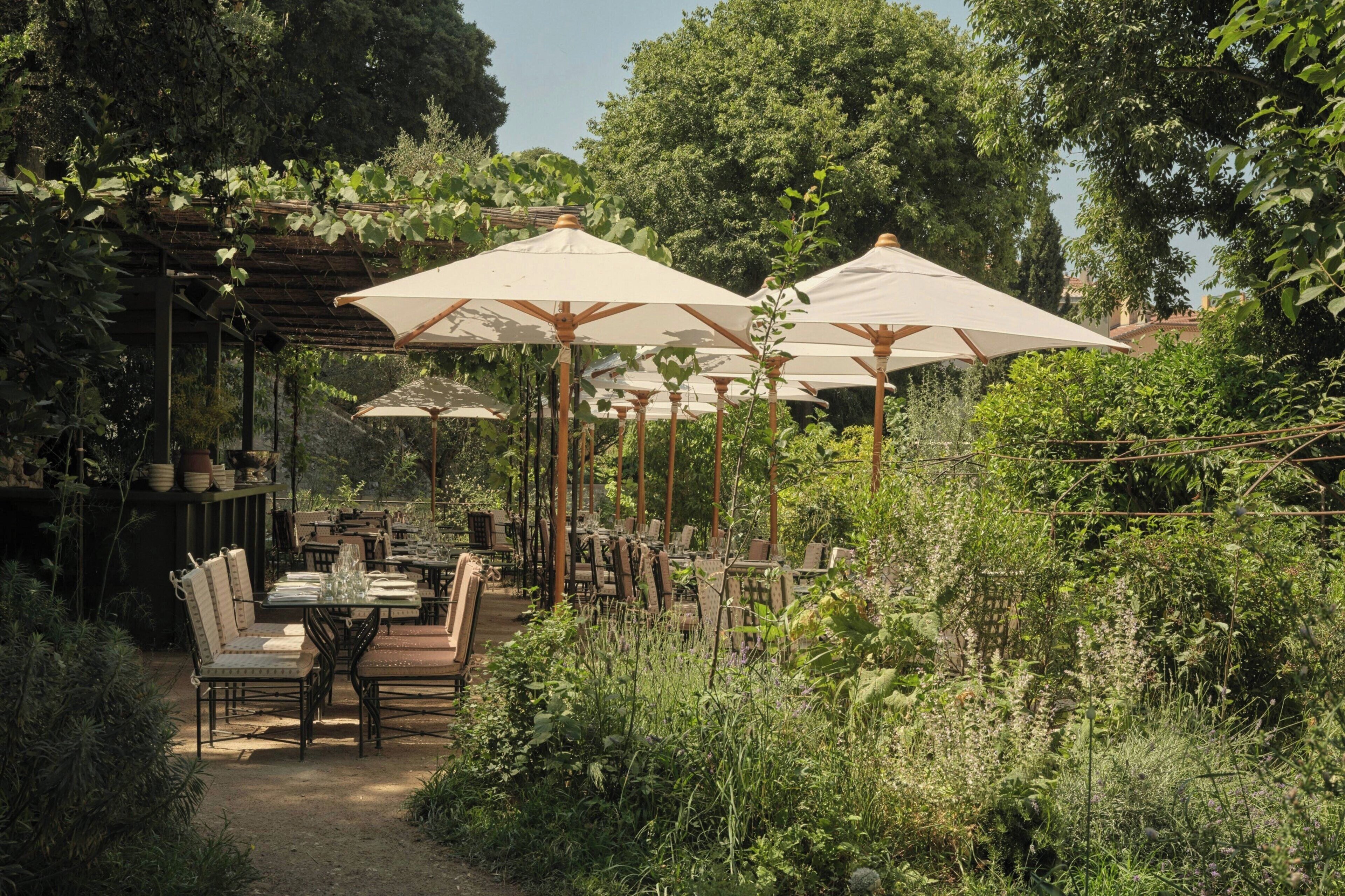 Een buitenterras met tafels en stoelen onder parasols, omgeven door weelderige begroeiing.