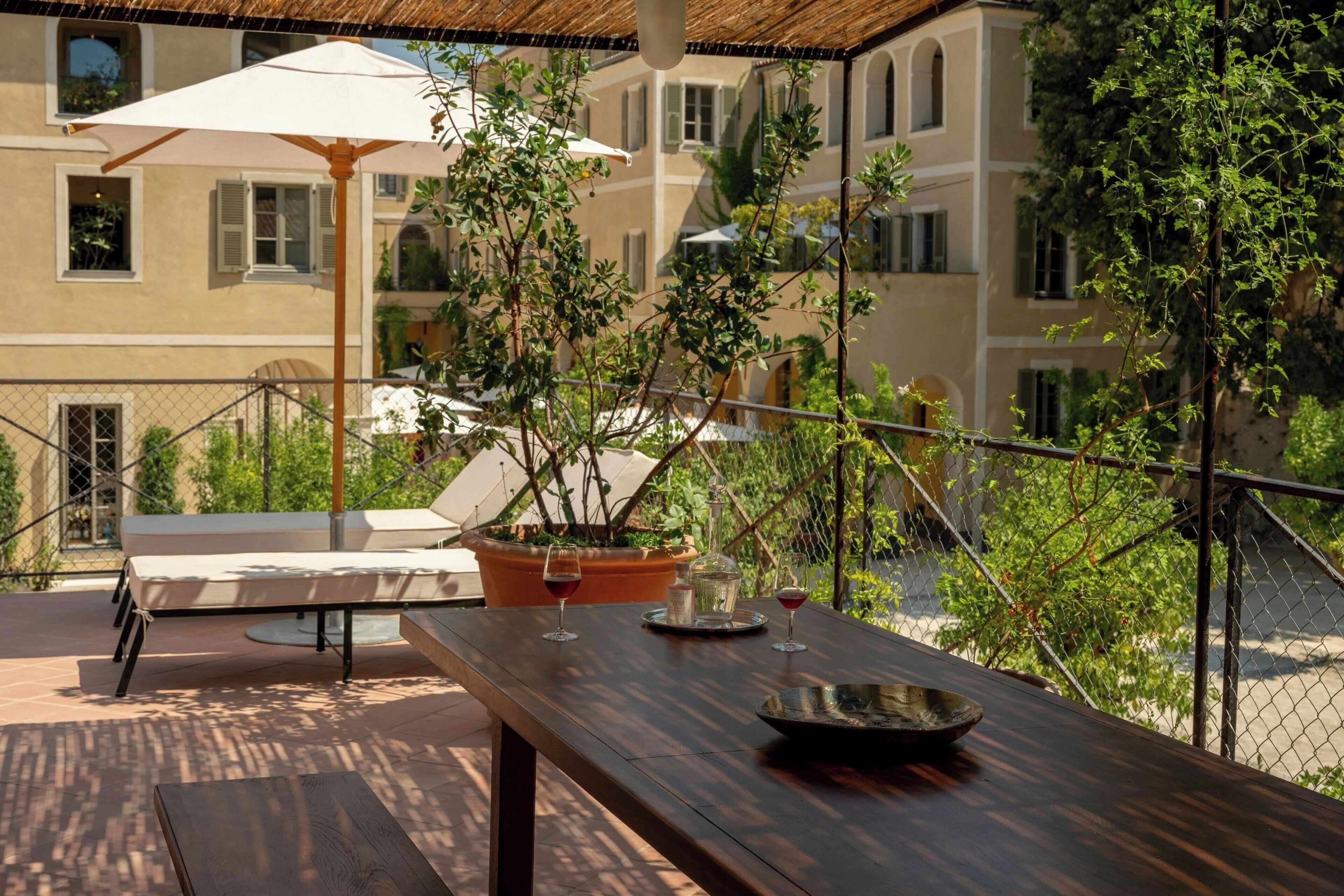 Un patio al aire libre con una mesa de madera, dos sillones, una planta en maceta y un paraguas blanco.