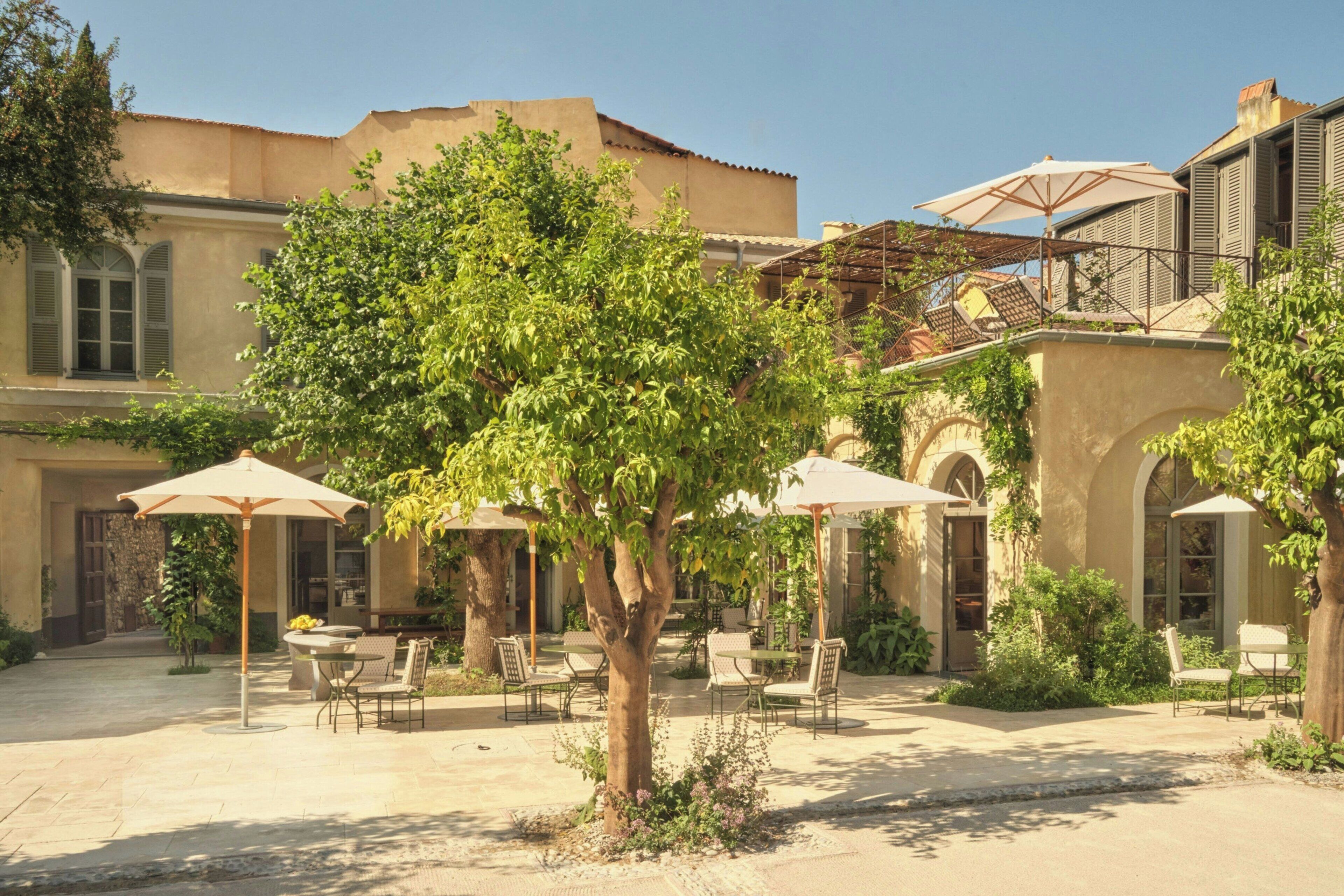 A courtyard with outdoor seating, trees, and a building with arches and a balcony.