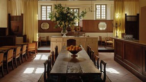 A dining area with a long wooden table, chairs, a vase with flowers, and a fruit bowl.