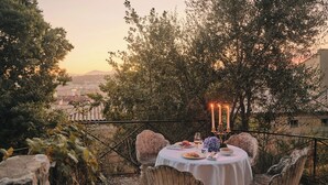 An outdoor dining area with a table set for two, surrounded by stone chairs, overlooking a cityscape at sunset. - Hotel Du Couvent, A Luxury Collection Hotel, Nice,  France (Nice)