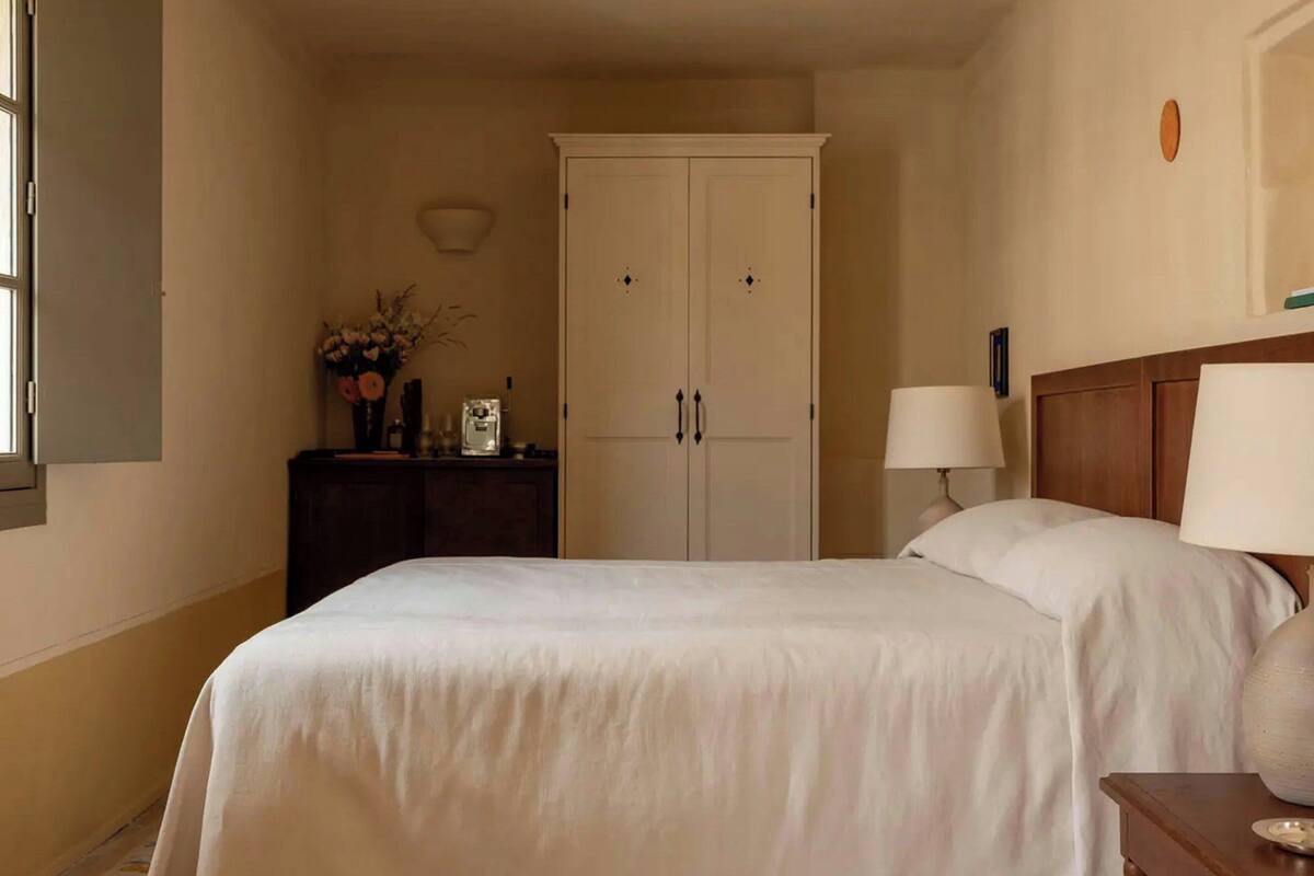 A bedroom with a bed, a nightstand, a lamp, a dresser, and a wardrobe.