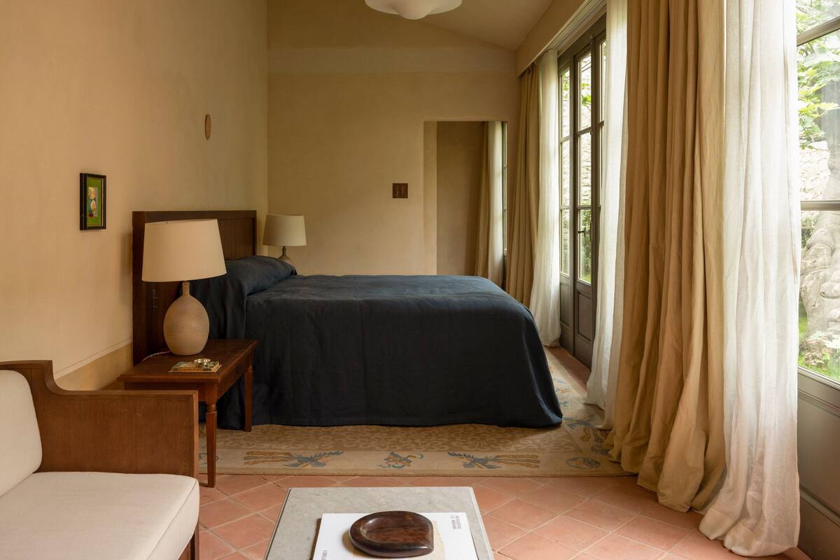 A hotel room with a bed, a nightstand, a lamp, a chair, and a window with curtains.