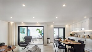 A modern living room with a sofa, a dining table with chairs, and a kitchen area with cabinets and a countertop.
