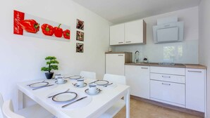 A modern kitchen with white cabinets, a microwave, and a sink. There is a dining table set with plates, cutlery, and a small potted plant. - Holiday apartment with air conditioning (Dramalj)