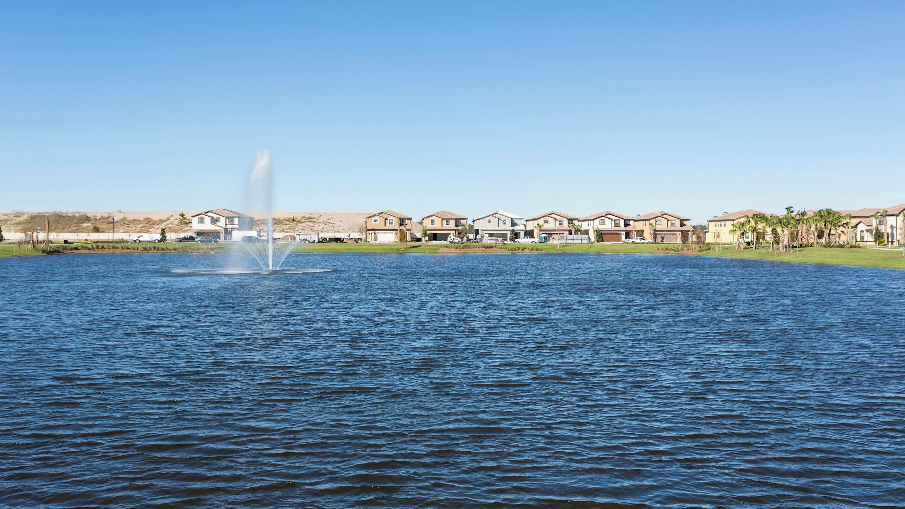A residential area with houses by a lake, a fountain, and a clear sky.