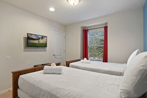 Une chambre d’hôtel avec deux lits, un téléviseur fixé au mur, une porte et une fenêtre avec des rideaux rouges.