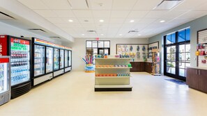 L’intérieur d’un magasin présente des distributeurs de boissons réfrigérés, des étagères remplies de divers produits et un présentoir situé au centre.