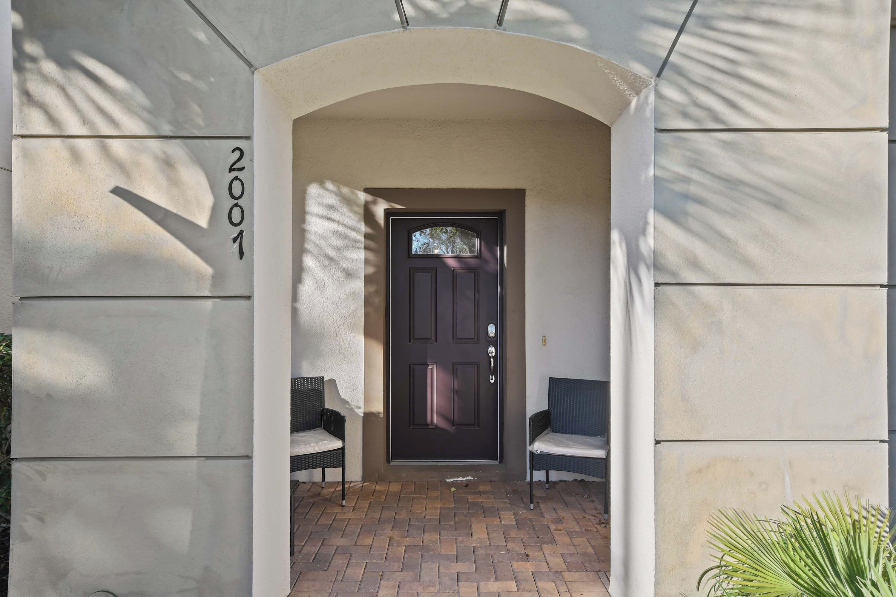 A building entrance with a dark door, two wicker chairs, and a brick pathway.