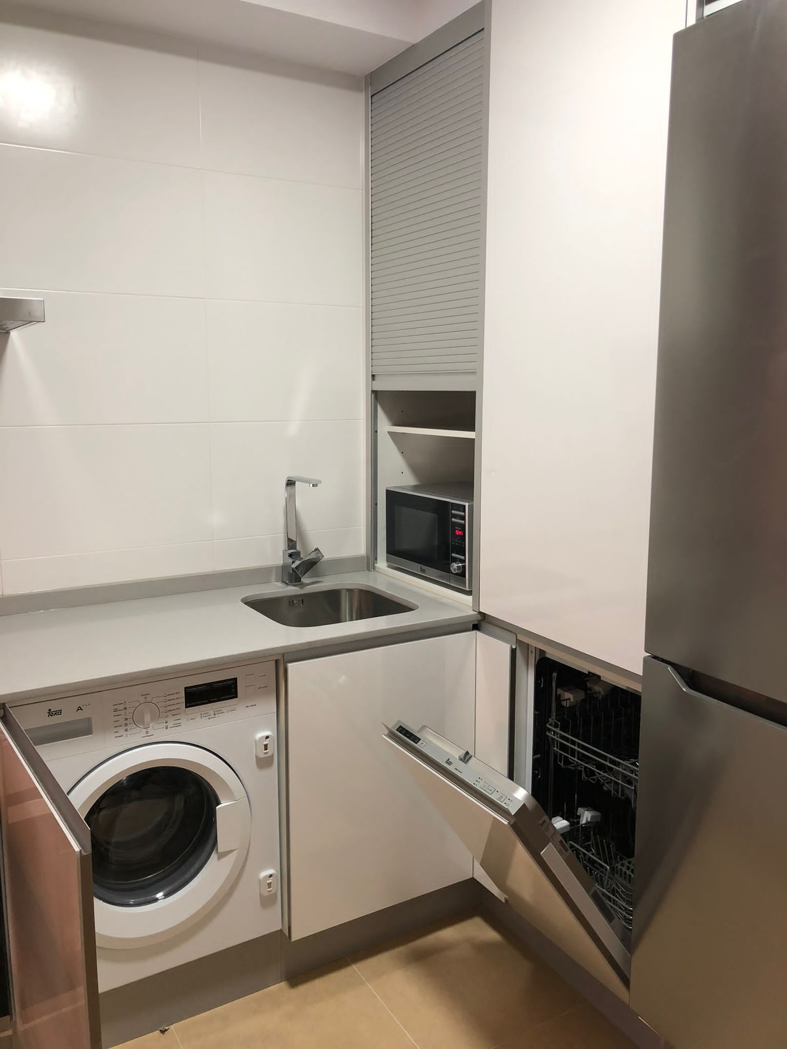 Eine kleine Küche mit Waschmaschine, Mikrowelle und Kühlschrank.