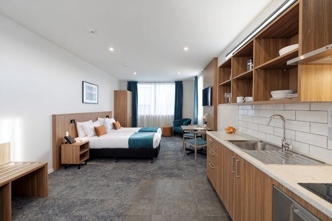 Ein modernes Hotelzimmer mit Bett, Schreibtisch und Küchenzeile.