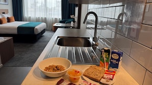 A hotel kitchen with a sink, breakfast items, and a sign with induction cooktop instructions. - Quest on Kilmore (Christchurch)