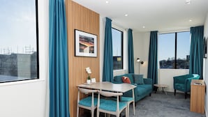 A modern living room with a wooden accent wall, a teal sofa, a small table, and a chair. - Quest on Kilmore (Christchurch)