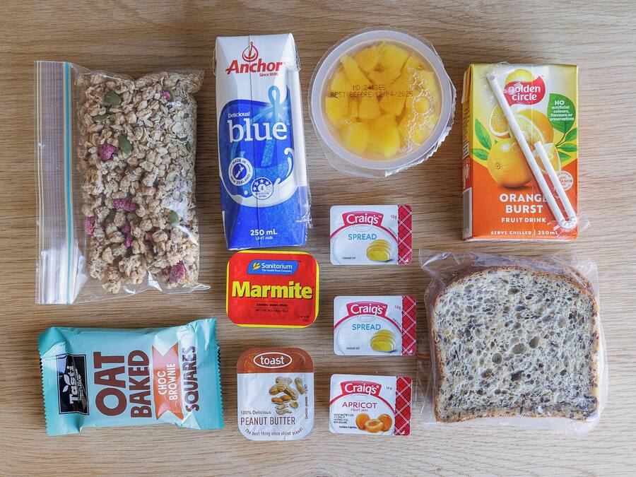A variety of food items including cereal, milk, fruit juice, bread, and spreads on a wooden surface.